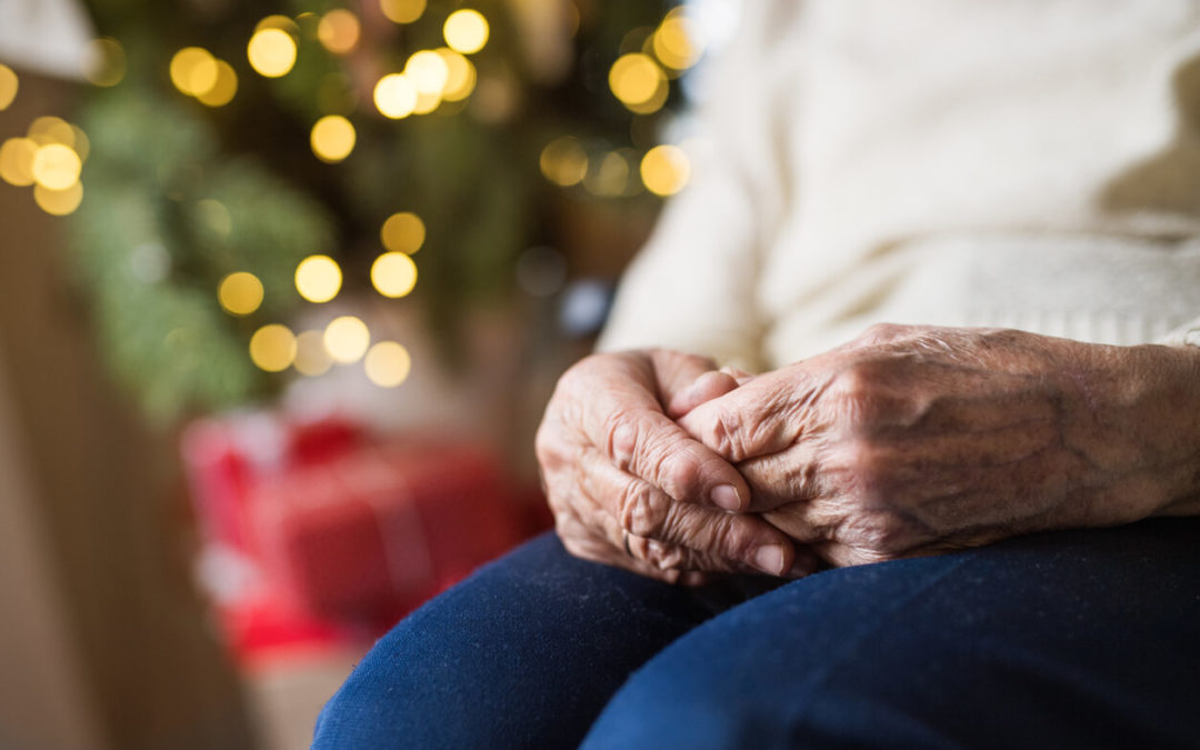 A close-up of hands and knees of an unrecognizable lonely senior woman sitting on an armchair at home at Christmas time.